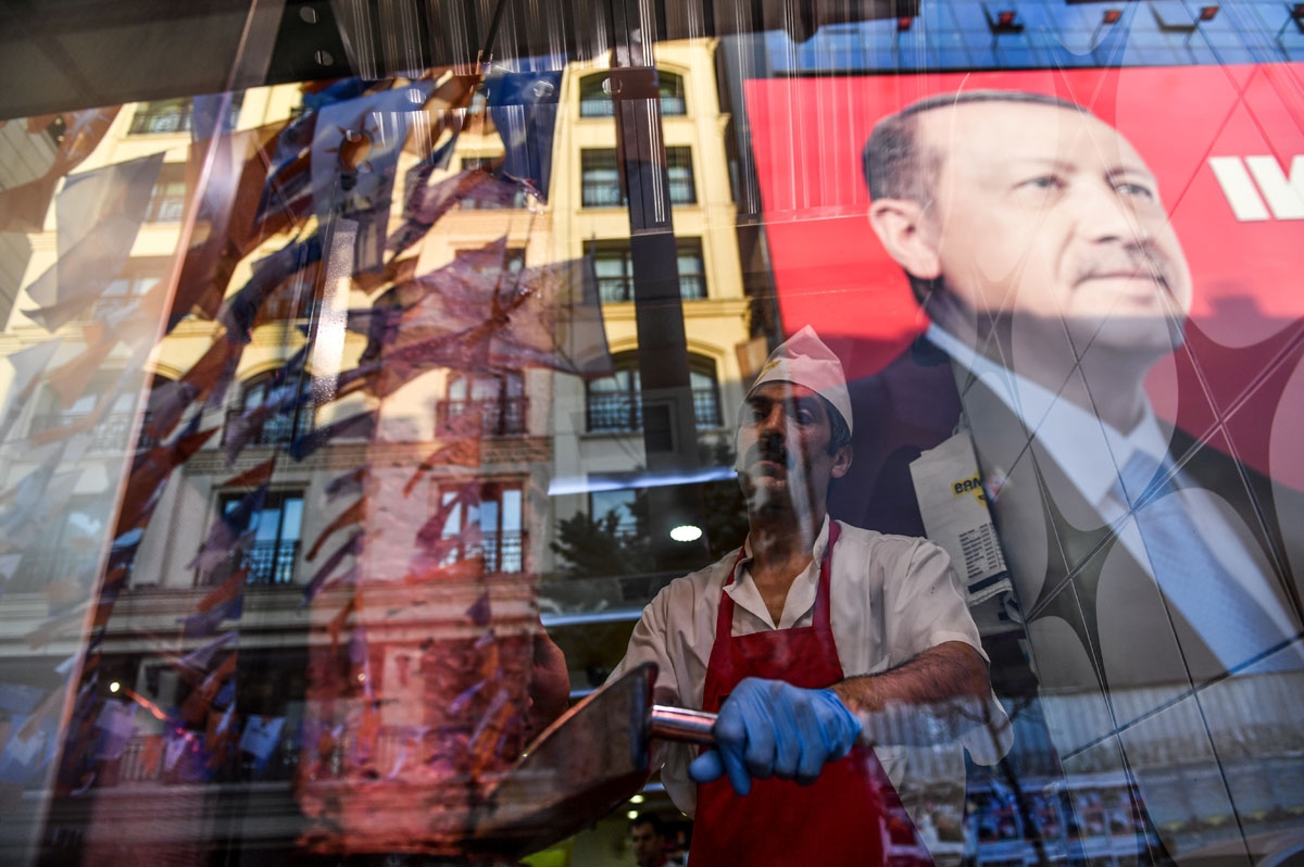 A worker slices meat as he stands in the window of a Turkish restaurant under a portrait of Turkish President Recep Tayyip Erdogan on Taksim Square in Istanbul on June 20, 2018.