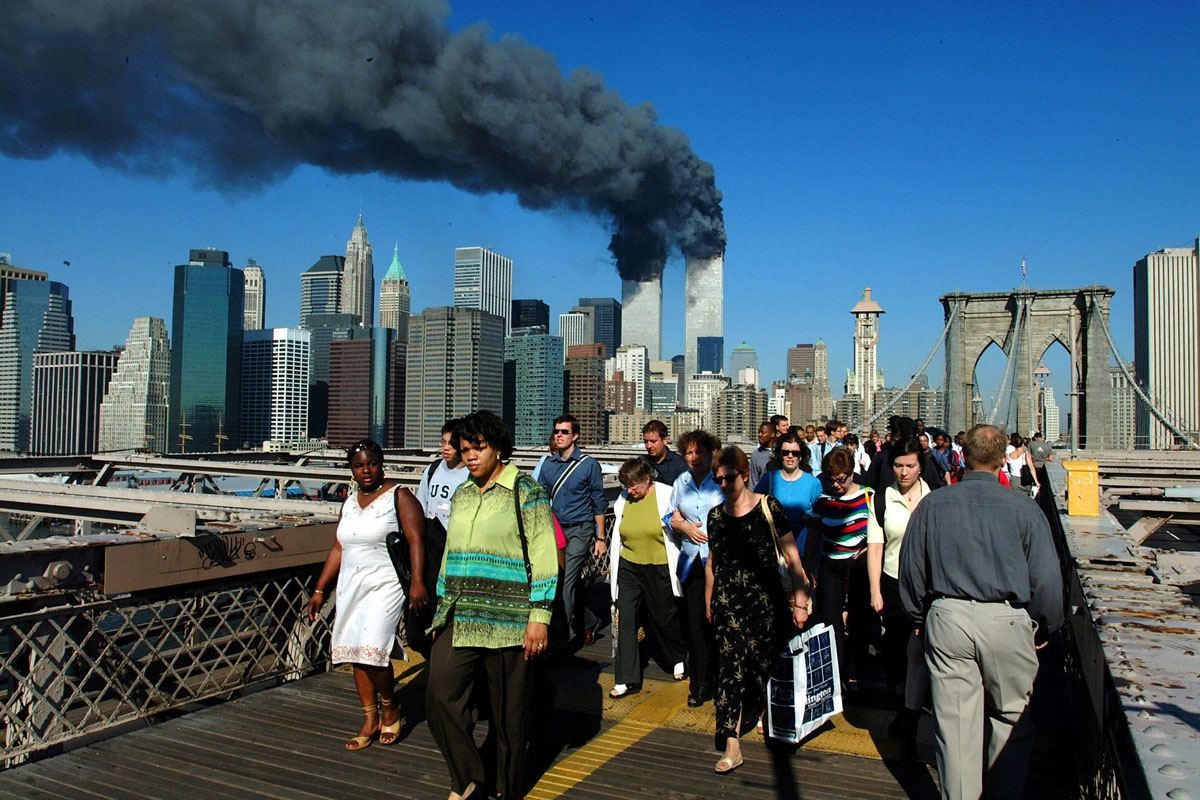 Pedestrians walk across the Brooklyn Bridge away from the burning World Trade towers before their collapse 11 September, 2001