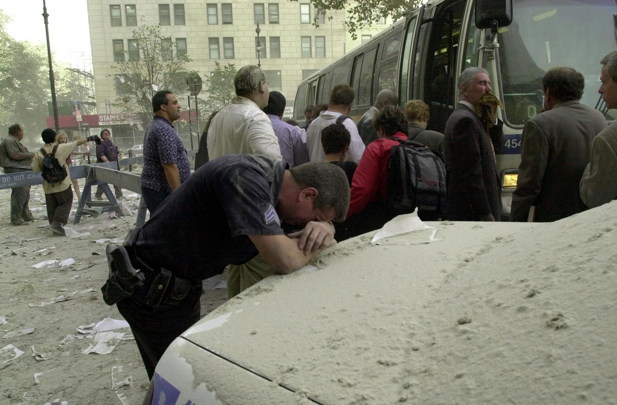 An exausted police officer rests on a car covered in dust near the World Trade Center 11 September 2001 in New York
