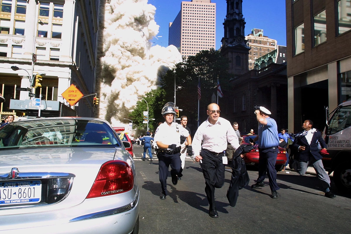 Police and pedestrians run for cover during the first collapse of the World Trade Center Tower after the landmark skyscrapers were struck by two hijacked airplanes 11 September 2001
