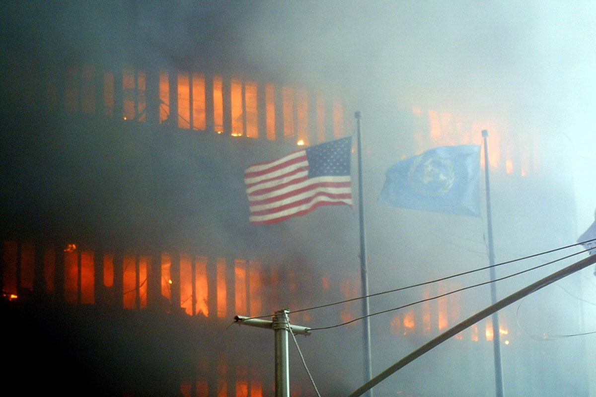 An American flag flies in the foreground as one of the World Trade Center towers burns in the background 11 September 2001 in New York.