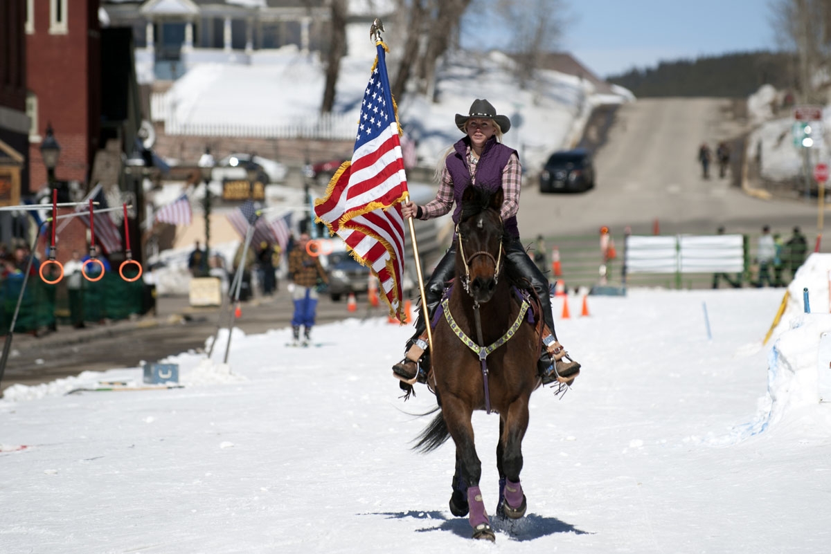 Flag bearer Jesslyn Swirka rides her horse down Harrison Avenue in Leadville, Colorado at the start of the 68th annual Leadville Ski Joring weekend competition on Saturday, March 4, 2017 in Leadville, Colorado.