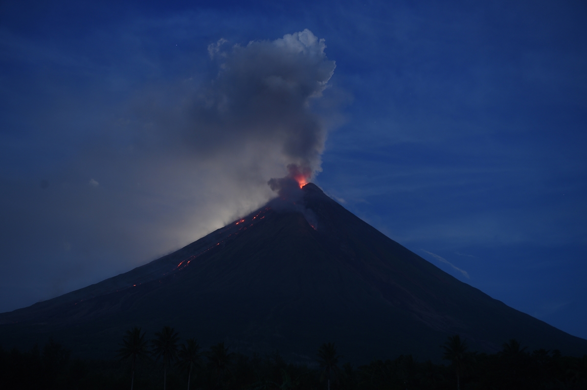 The 'super blue blood moon' obscured by clouds illuminates Mayon volcano as it spews ash near Legazpi City, Albay province, early on February 1, 2018.