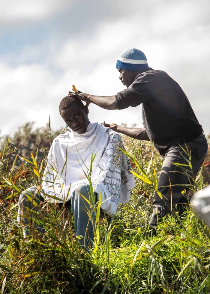 A migrant cuts a fellow refugee's hair A migrant cuts a fellow refugee's hair