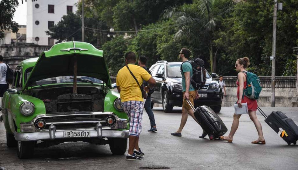 A man fixes his car as tourists walk past in Havana, March, 2016. A man fixes his car as tourists walk past in Havana, March, 2016.