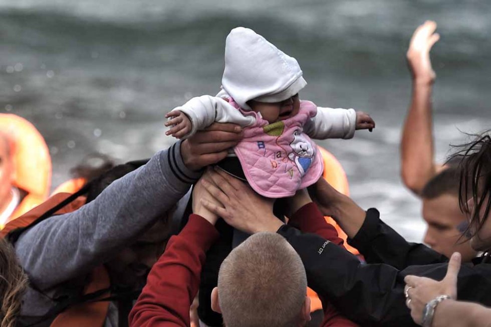 A baby is passed from hand to hand after arriving in Lesbos in late October. A baby is passed from hand to hand after arriving in Lesbos in late October.
