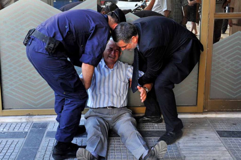 A July 3, 2015 photograph shows Greek pensioner Giorgos Chatzifotiadis being assisted by a bank employee and a policeman outside a bank branch in Thessaloniki (AFP PHOTO /SAKIS MITROLIDIS) A July 3, 2015 photograph shows Greek pensioner Giorgos Chatzifotiadis being assisted by a bank employee and a policeman outside a bank branch in Thessaloniki (AFP PHOTO /SAKIS MITROLIDIS)