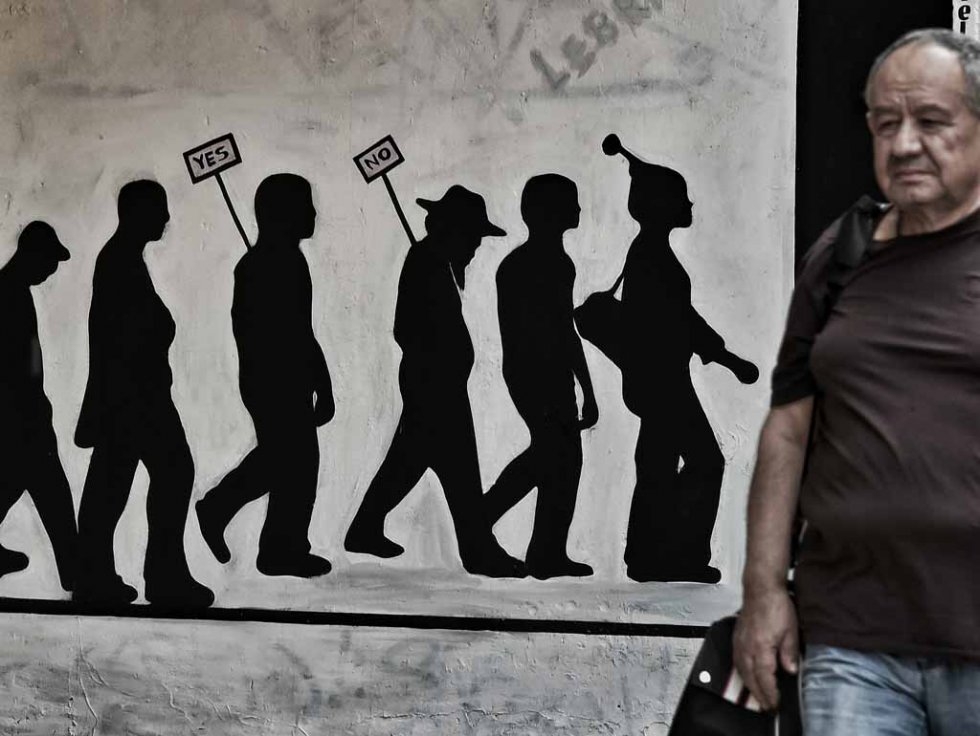 A man walks past a wall bearing graffitti concerning the Greek referendum a debt deal with its EU-IMF creditors in Athens on June 28, 2015 A man walks past a wall bearing graffitti concerning the Greek referendum a debt deal with its EU-IMF creditors in Athens on June 28, 2015