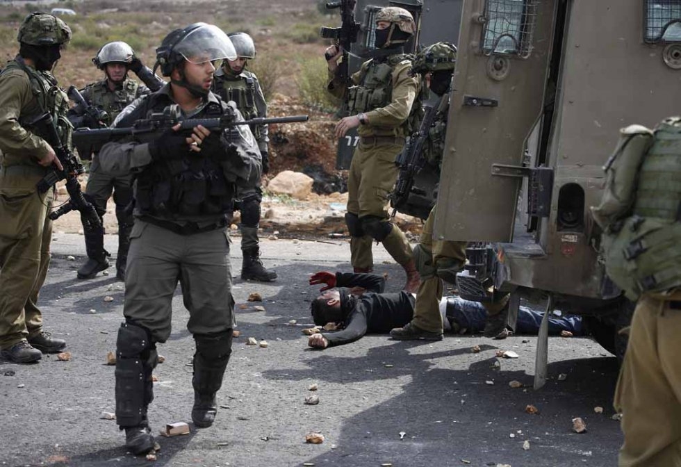 Israeli soldiers and border guards stand next to a wounded Palestinian stone thrower who was shot by infiltrated members of the Israeli security forces during clashes in Beit El on October 7, 2015 (AFP / Abbas Momani) Israeli soldiers and border guards stand next to a wounded Palestinian stone thrower who was shot by infiltrated members of the Israeli security forces during clashes in Beit El on October 7, 2015 (AFP / Abbas Momani)
