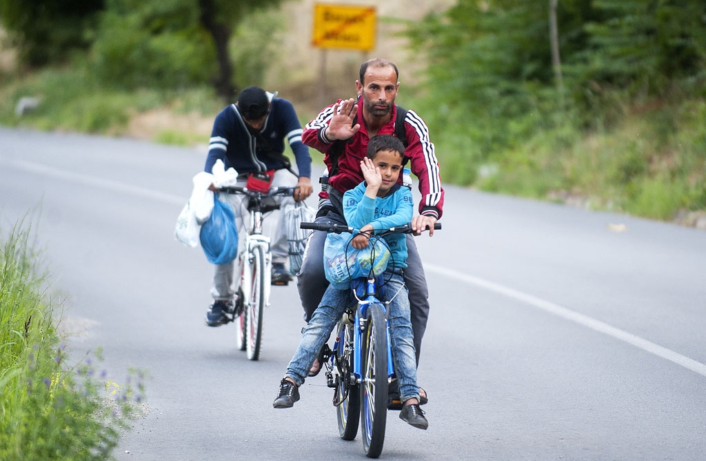 A migrant and his son ride a bicycle on a highway near the town of Veles on June 9, 2015 A migrant and his son ride a bicycle on a highway near the town of Veles on June 9, 2015