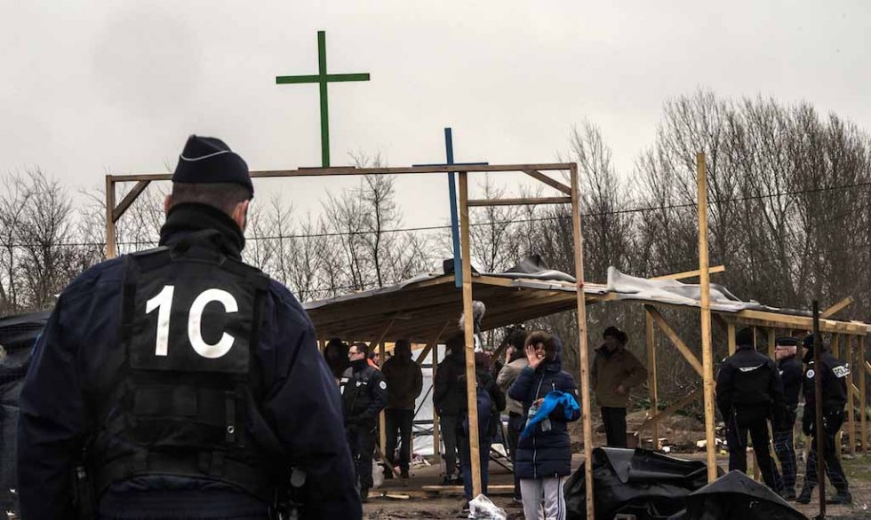 A French riot policeman stands guard during demolition of makeshift structures in the Jungle, including a church and a mosque. February, 2016. A French riot policeman stands guard during demolition of makeshift structures in the Jungle, including a church and a mosque. February, 2016.