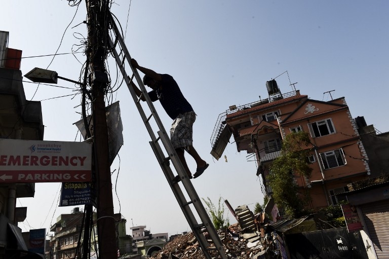 A Nepalese man climbs down a ladder in Kathmandu on May 1, 2015, after fixing some wiring near a house left precariously standing after the April 25 quake A Nepalese man climbs down a ladder in Kathmandu on May 1, 2015, after fixing some wiring near a house left precariously standing after the April 25 quake