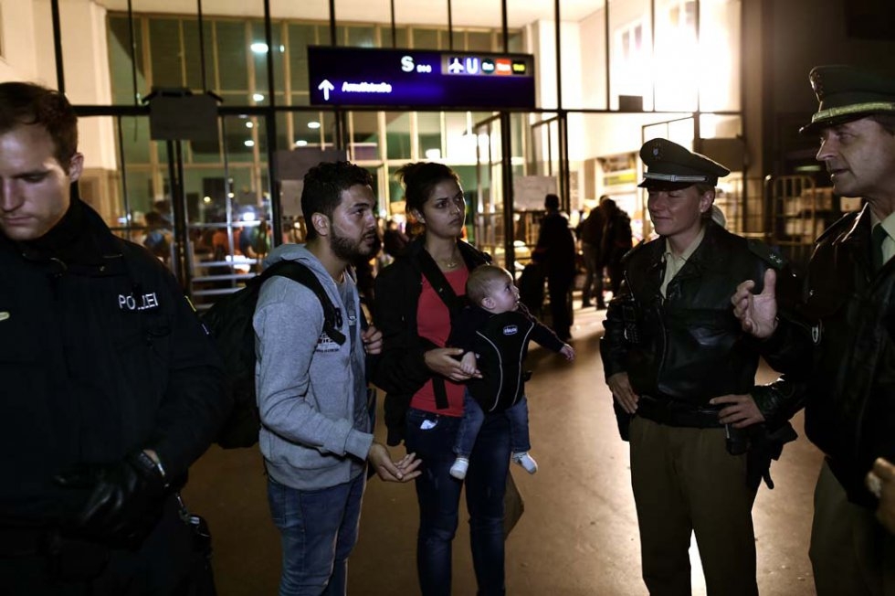 Iraqi refugees Ahmad, Alia and their four months old baby Adam, talk with German police officers after arriving in Munich on September 3, 2015 Iraqi refugees Ahmad, Alia and their four months old baby Adam, talk with German police officers after arriving in Munich on September 3, 2015