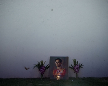 A lit candle and flowers adorn an image of the late Thai King Bhumibol Adulyadej on the outer wall of the Grand Palace at dawn on October 16, 2016. 