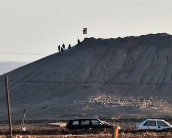 Alleged Islamic State group militants stand next to an IS flag atop a hill in the Syrian town of Kobane, as seen from the Turkish-Syrian border (AFP Photo / Aris Messinis)