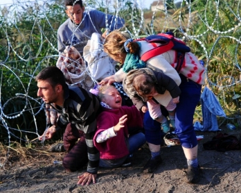 A family crawls under the Hungarian-Serbian border fence near Roszke on August 27, 2015 (AFP Photo / Attila Kisbenedek)