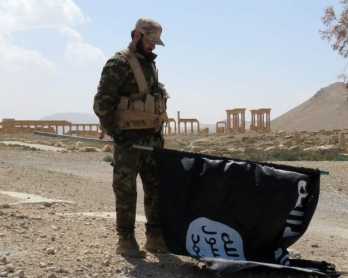 A member of the Syrian pro-government forces carries an Islamic State (IS) group flag in the ancient city of Palmyra on March 27, 2016 (AFP)